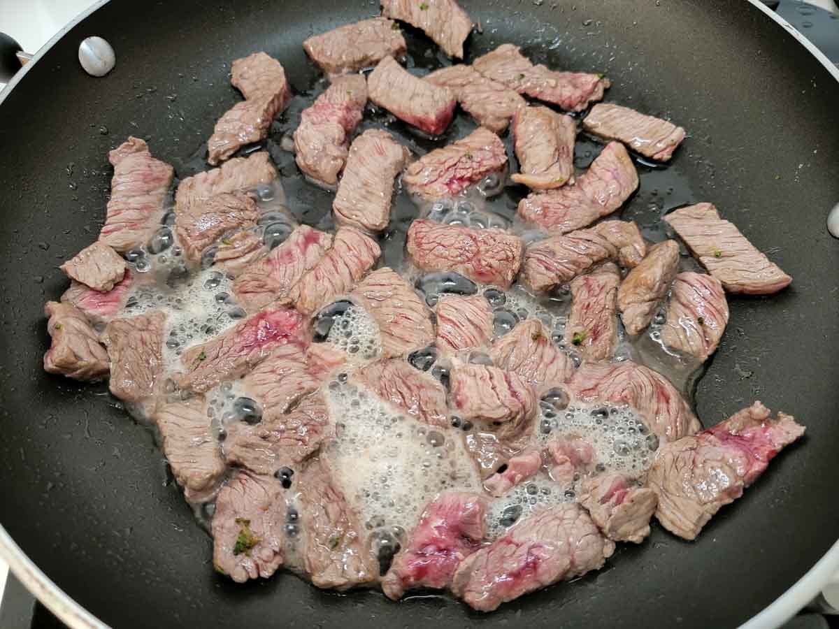 sirloin steak slices cooking in a frying pan.