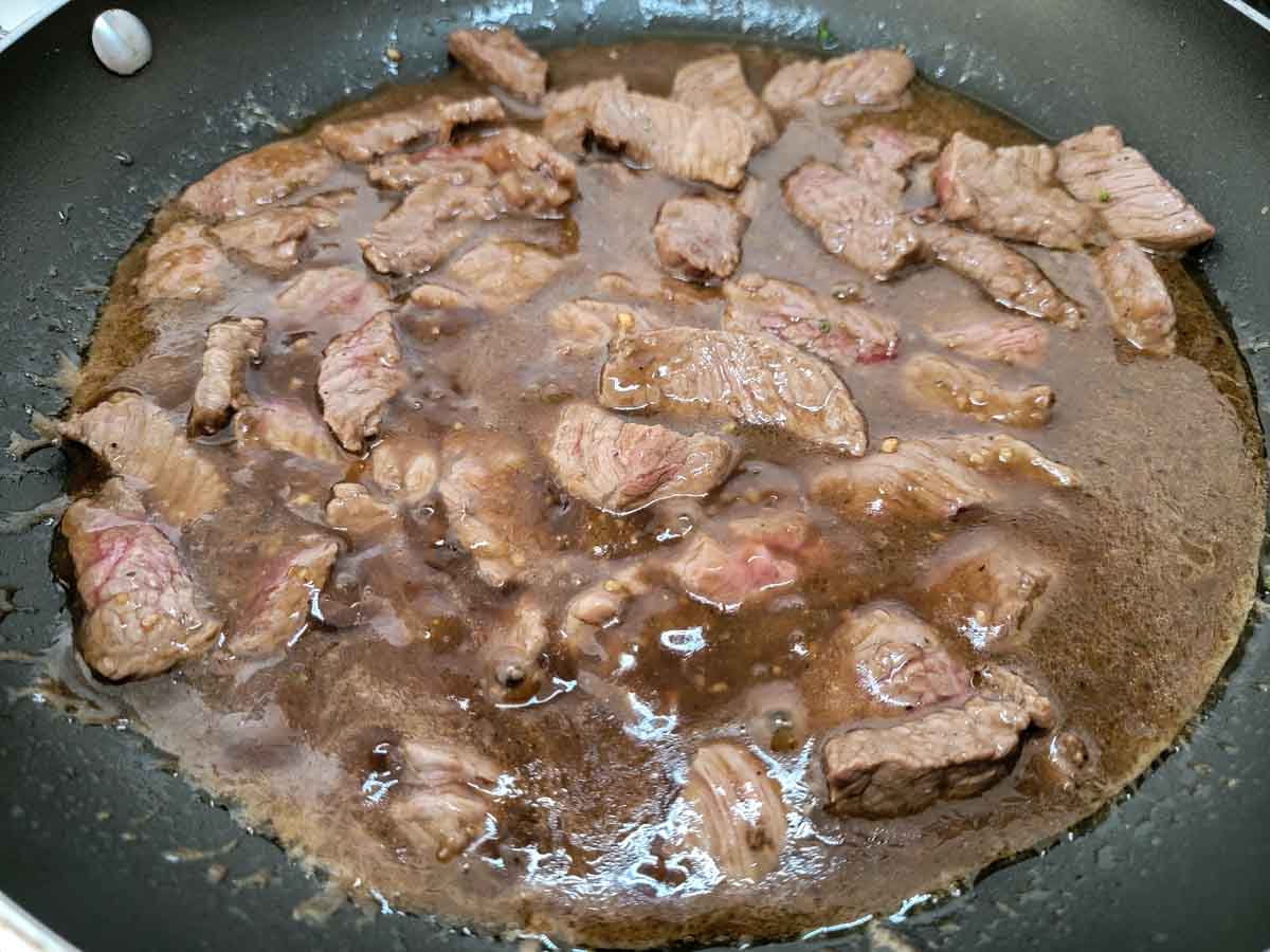 sirloin steak and brown sauce cooking in a pan.