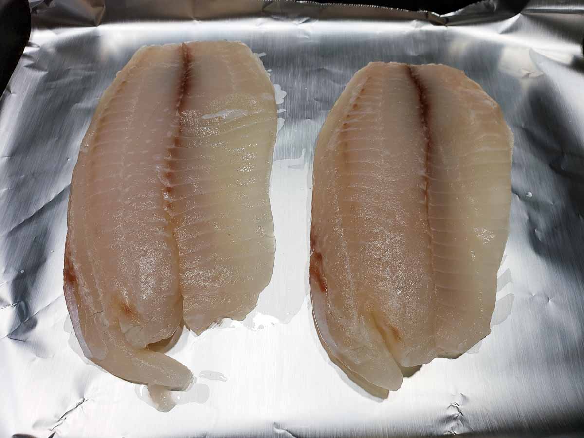 tilapia fillets on a baking sheet lined with tinfoil.