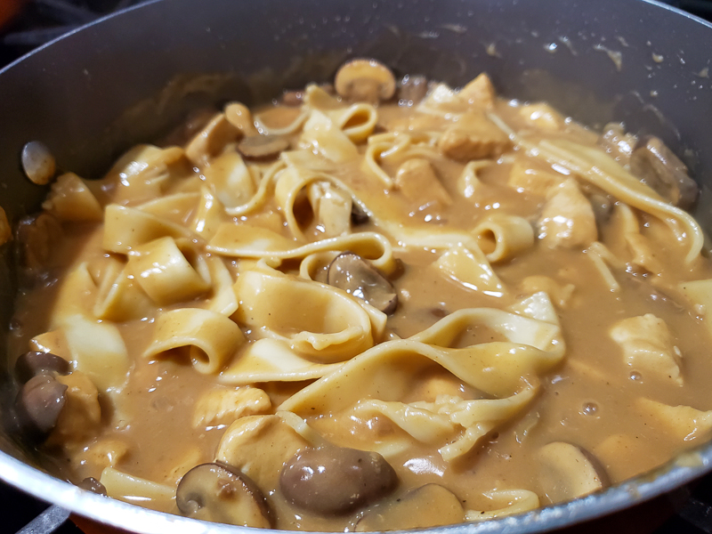 egg noodles added to the stroganoff cooking in the pan.