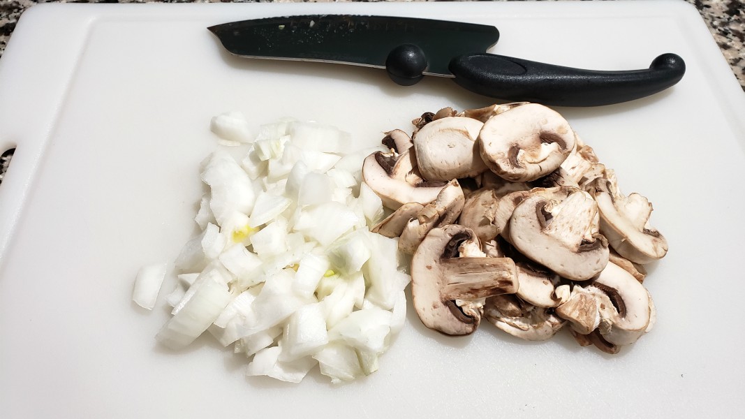 diced onions and sliced mushrooms on a cutting board.