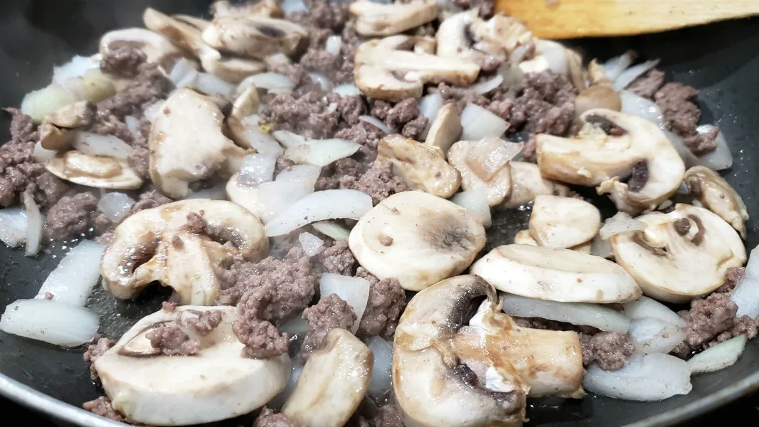 ground beef, mushrooms and onions cooking in a skillet.