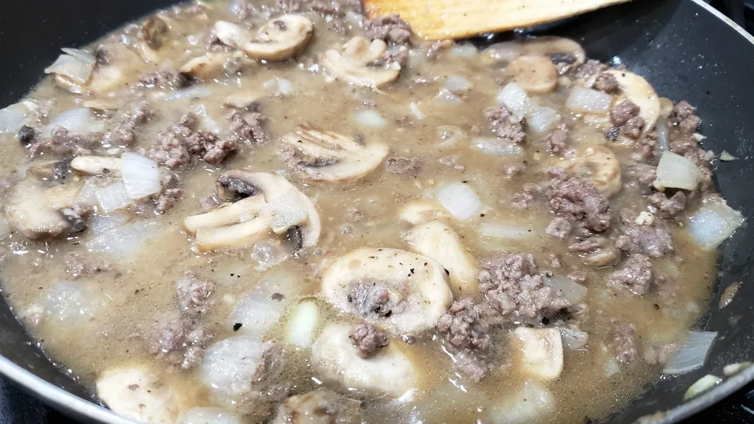 ground beef, mushrooms and onions in broth sauce cooking in a skillet.