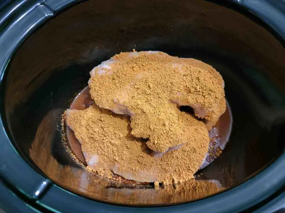 more taco seasoning sprinkled over chicken in a crockpot.