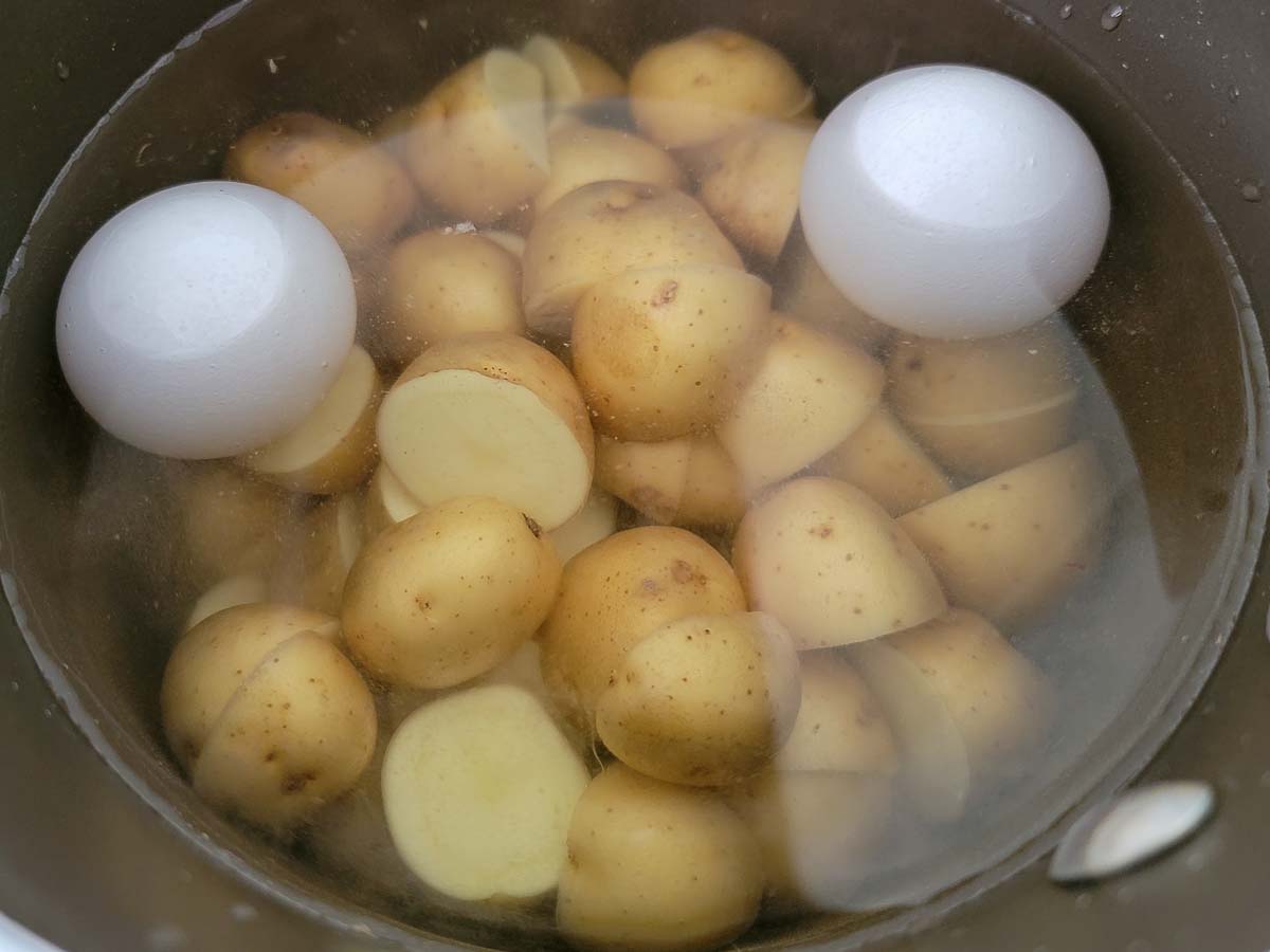 two eggs and baby potatoes in a pan of water.