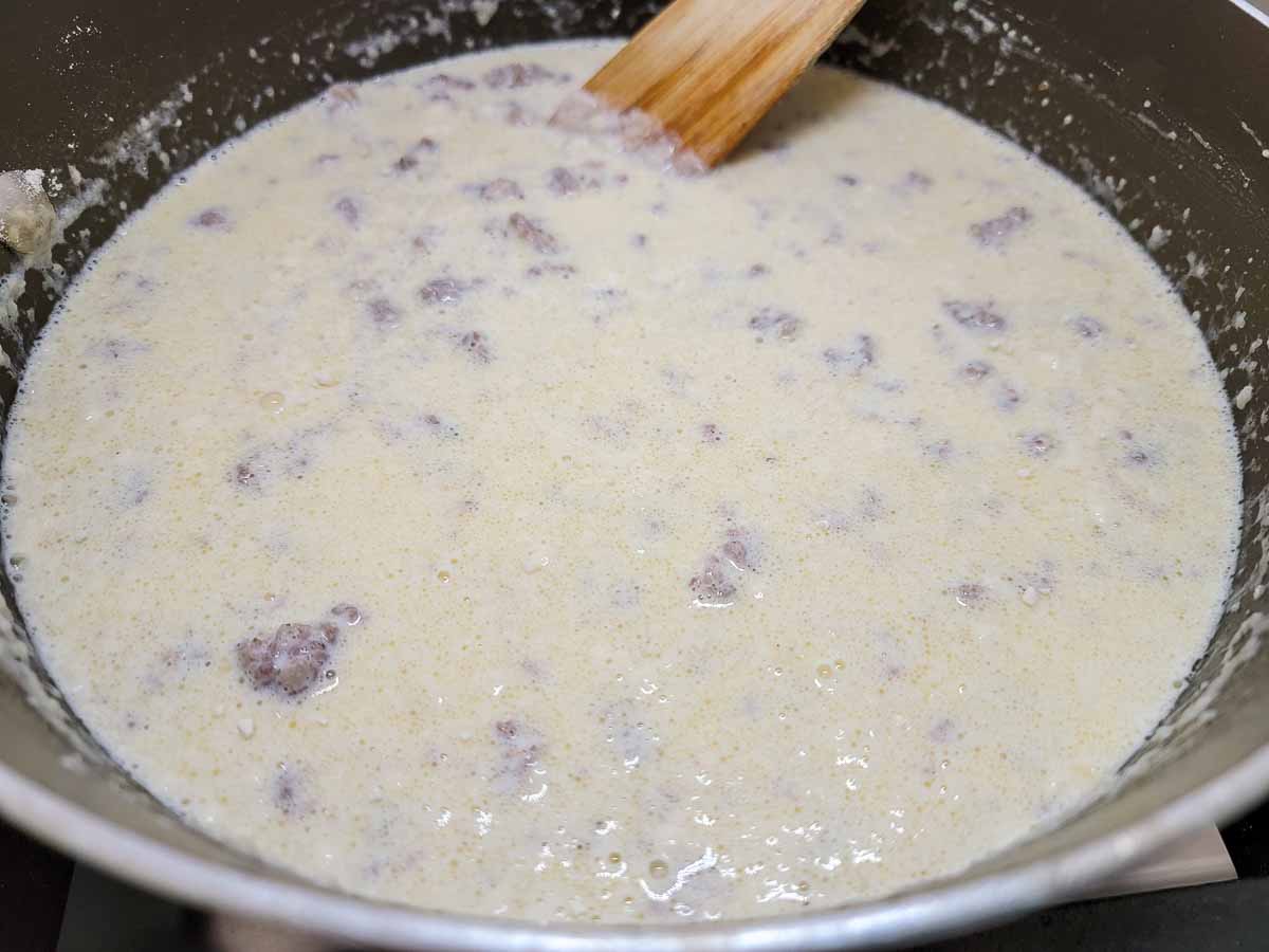 ground pork sausage, flour, butter, and cream cooking in a skillet.