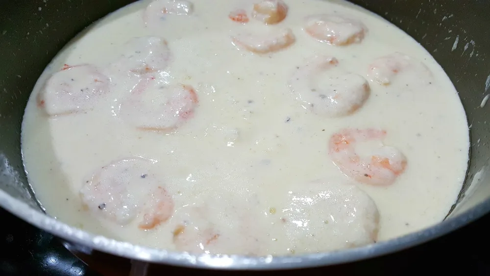 alfredo sauce with shrimp in it cooking in a pan.