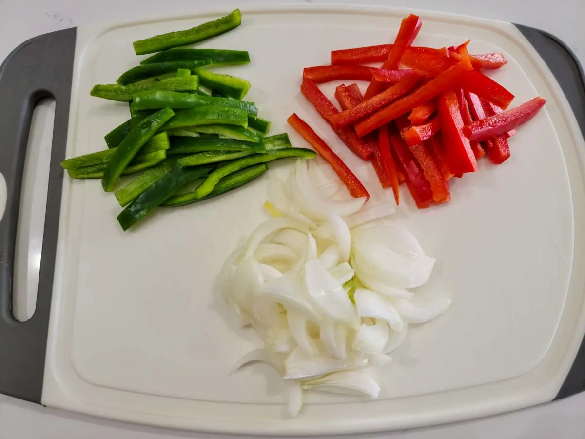 green pepper, red pepper and onion sliced on a cutting board.