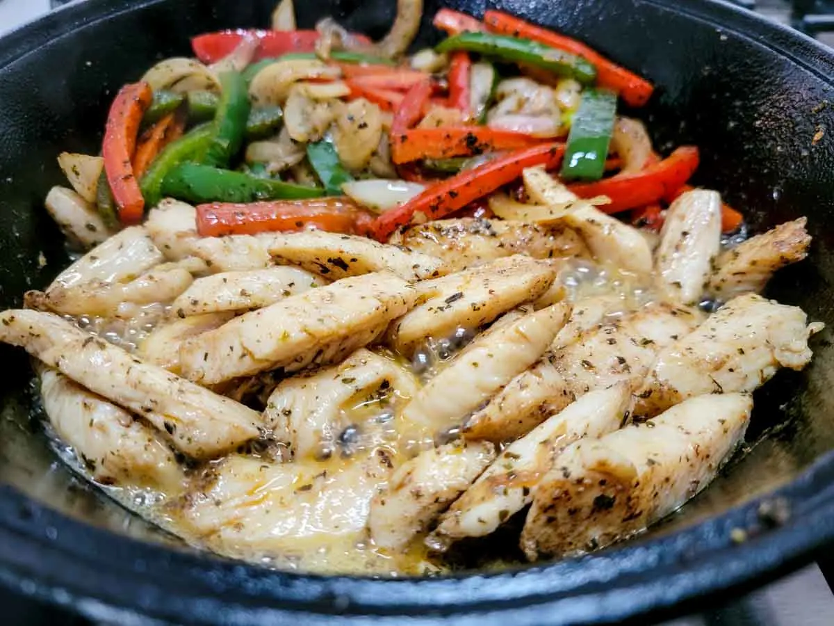 bell peppers, onions, chicken and seasoning cooking in a skillet.