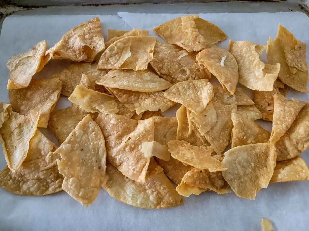 tortilla chips spread on a parchment lined baking sheet.