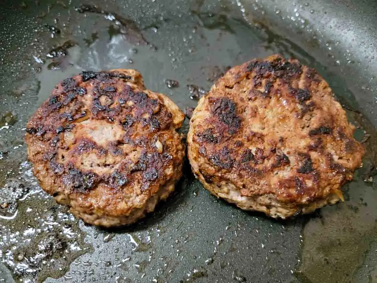 two browned turkey burgers frying in a pan.