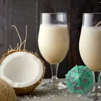 Pina Coladas with Malibu Rum in two tall glasses and a split open coconut on the side.