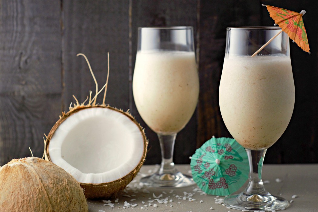Pina Coladas with Malibu Rum in two tall glasses and a split open coconut on the side.