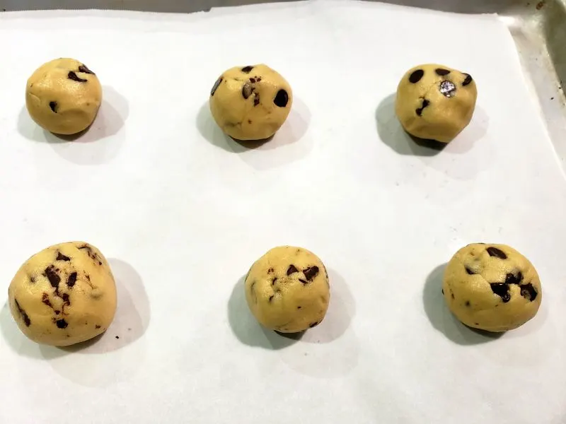 6 balls of cookie dough on parchment paper on a baking sheet.