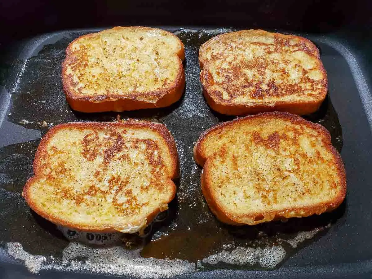 four french toast slices cooking in a skillet.