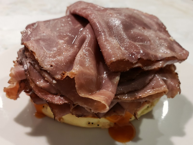 a sandwich bun bottom topped with roast beef and red ranch sauce.