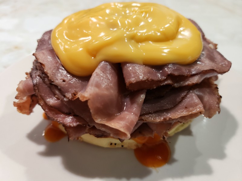 a sandwich bun bottom topped with cheddar cheese sauce, roast beef and red ranch sauce.