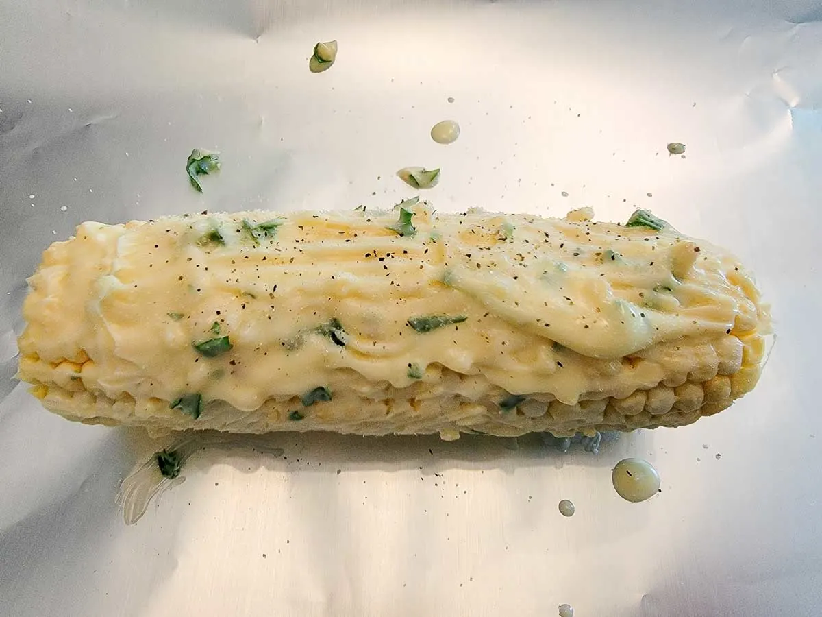 a raw corn cob slathered with butter mixture on a piece of foil.