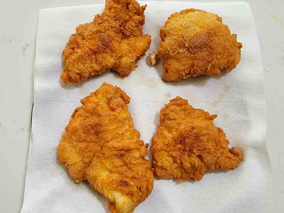 4 pieces of crispy fried boneless chicken draining on paper towel.