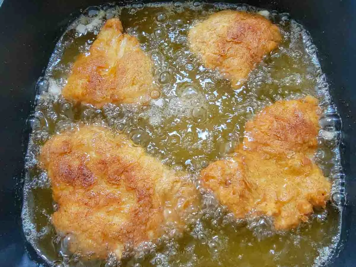 4 pieces of breaded chicken frying in oil.