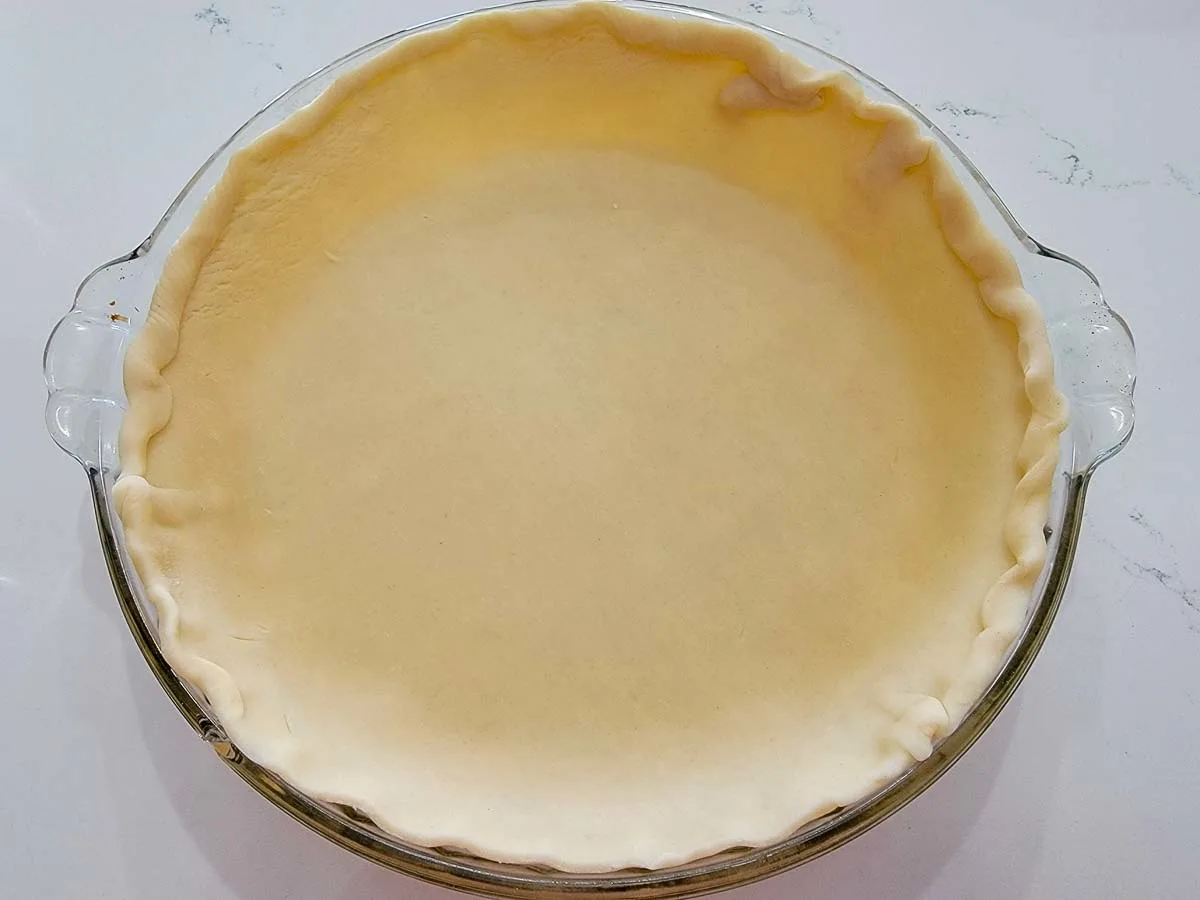 unbaked pie dough in a glass pie dish.