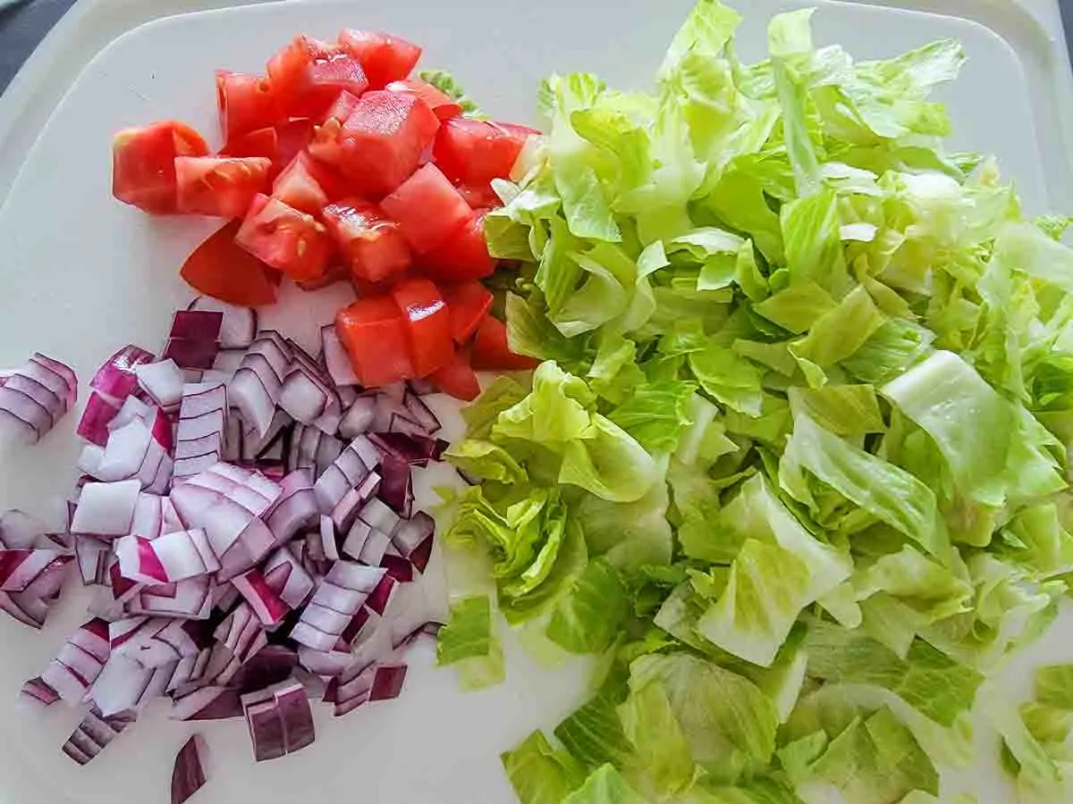 lettuce, tomato, and red onion chopped on a cutting board.