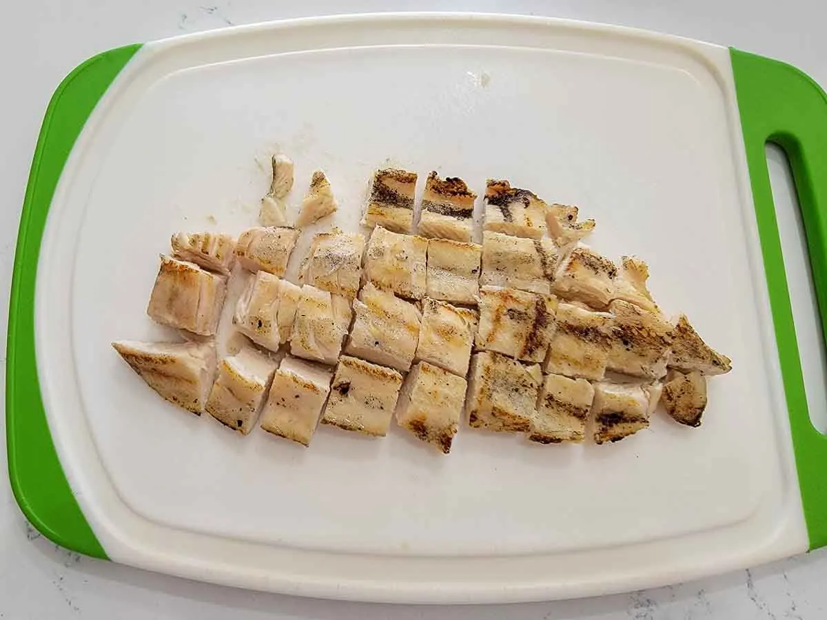grilled boneless chicken breast cut into bite sized pieces on a cutting board.