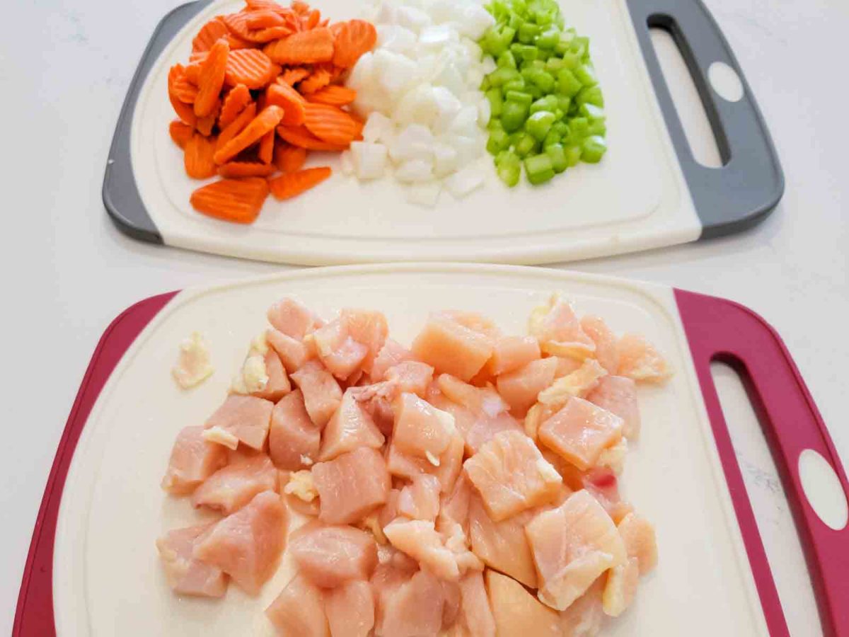 sliced carrots, diced onions, diced celery, and diced chicken on two cutting boards.
