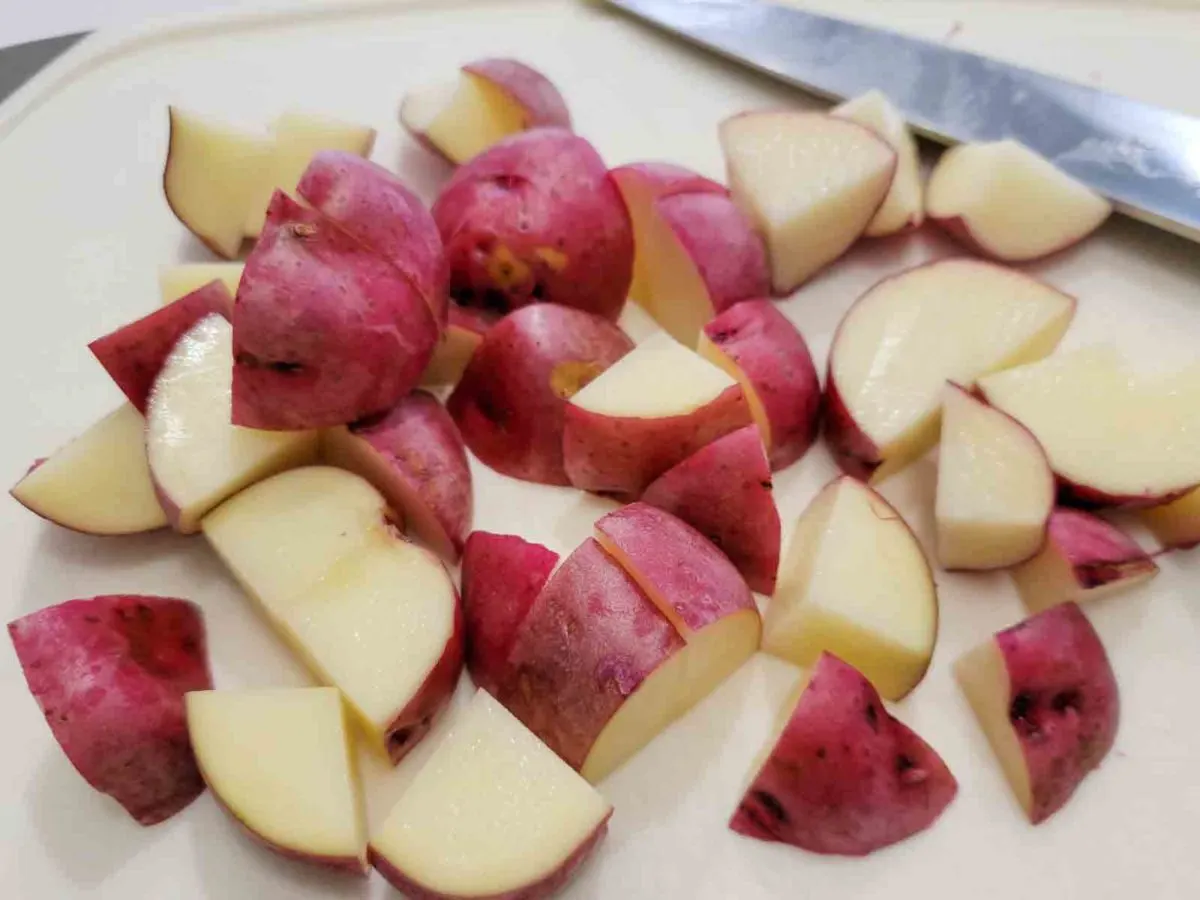 red skin potatoes cut into pieces on a cutting board.