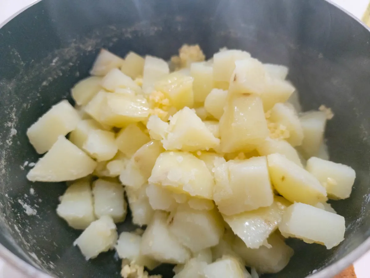 garlic, oil, and cooked diced potatoes in a pan.