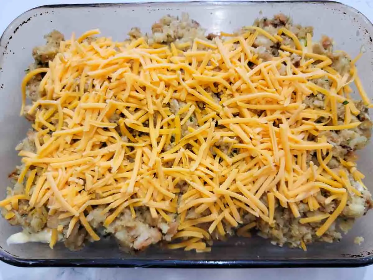 shredded cheese layered over stuffing in a baking dish.