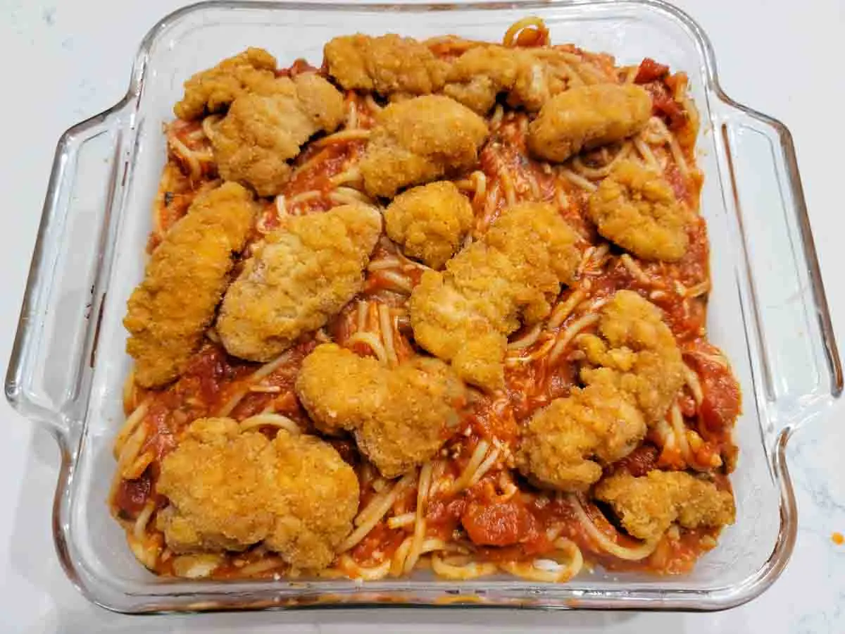 chicken nuggets over spaghetti in a baking dish.
