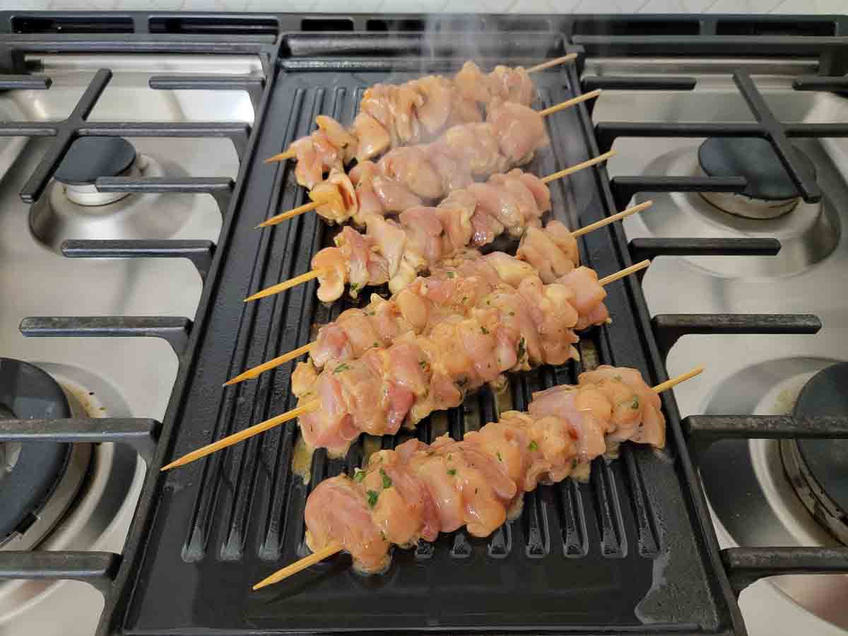 peanut chicken skewers cooking on a griddle.
