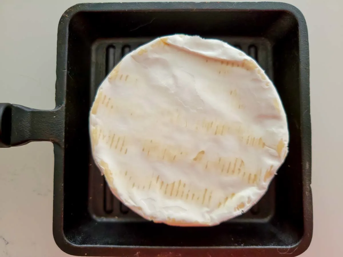 a wheel of unbaked brie cheese in a small cast iron dish.