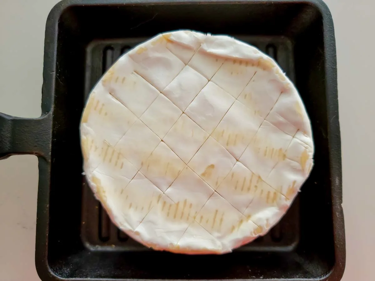 a wheel of unbaked brie cheese with criss-cross knife scores on top in a small cast iron dish.