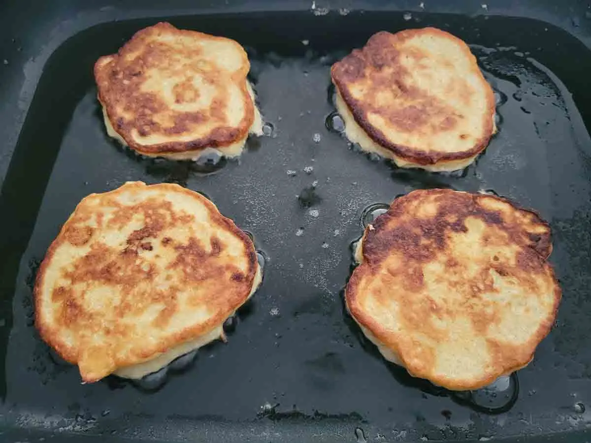 4 golden brown banana pancakes cooking in a skillet.
