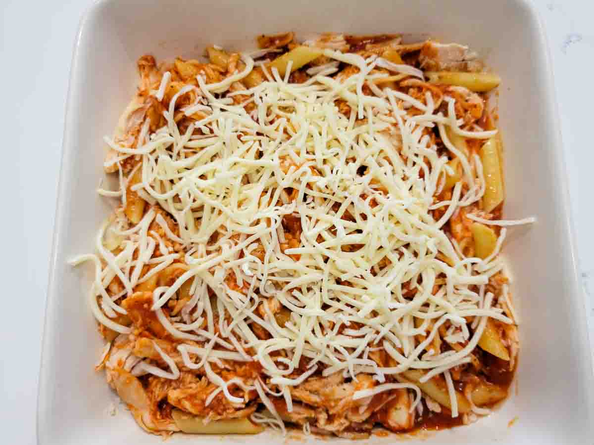 penne pasta, chicken, sauce, and mozzarella cheese in a baking dish.