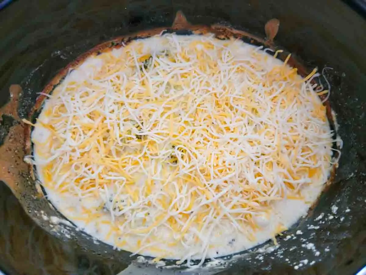 Crockpot Chicken Poppy Seed Casserole topped with cheese in a slow cooker.