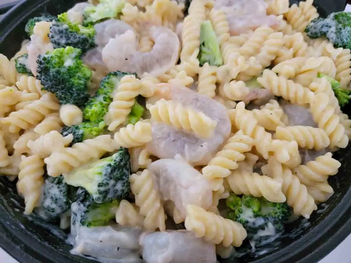 shrimp, broccoli, pasta, and cheese sauce mixed in a skillet.