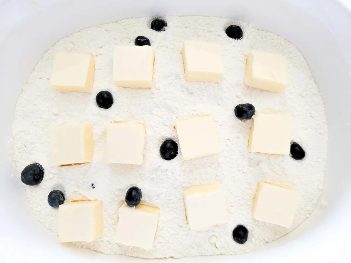 pats of butter, fresh blueberries, and dry cake mix over blueberries in a large dish.