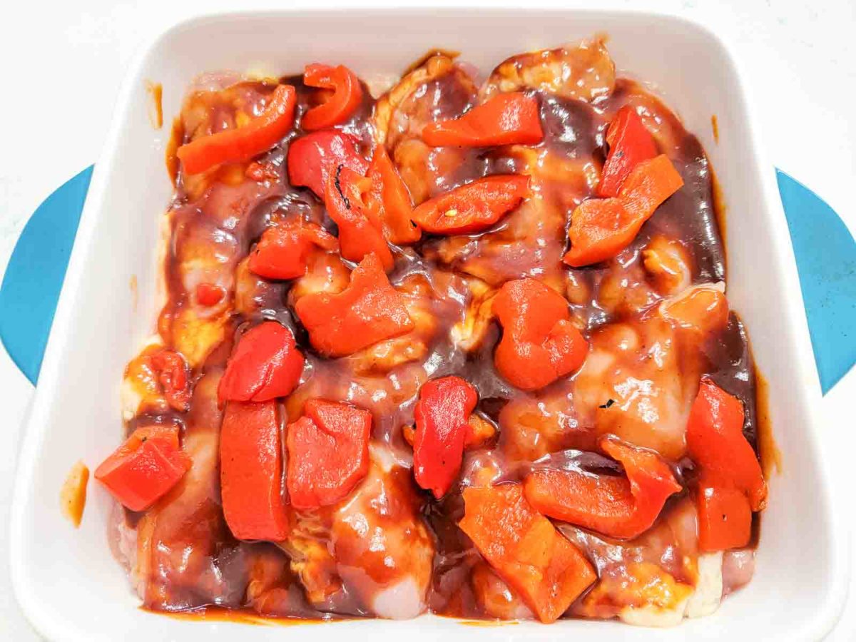 chicken thighs, roasted red peppers, and bbq sauce in a baking dish.