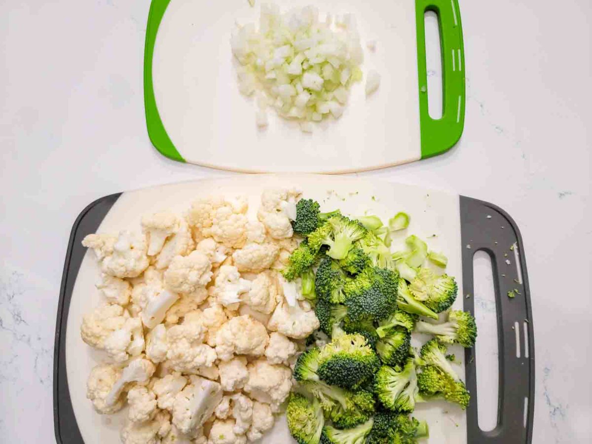 chopped broccoli, cauliflower, and onions on two cutting boards.