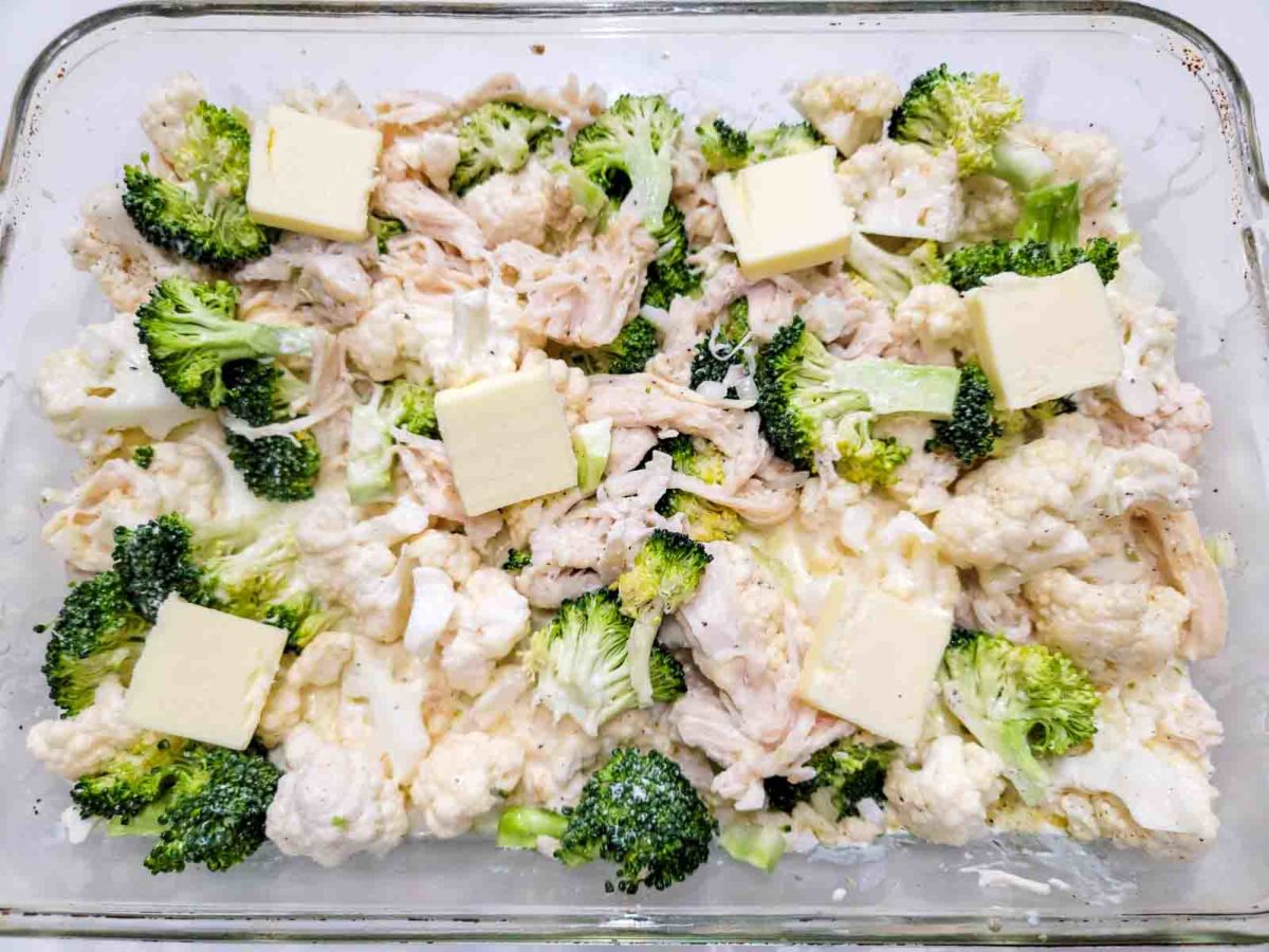 chicken broccoli cauliflower topped with butter pats in a baking dish.