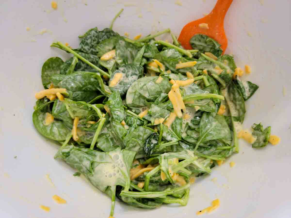 eggs, milk, salt, pepper, spinach leaves and cheddar cheese mixed in a bowl.