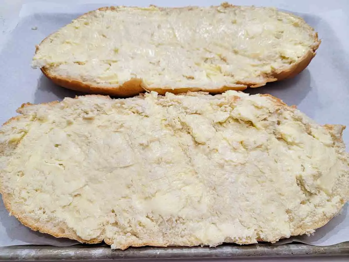 bread loaf sliced in half length wise slathered with garlic butter on a baking sheet.