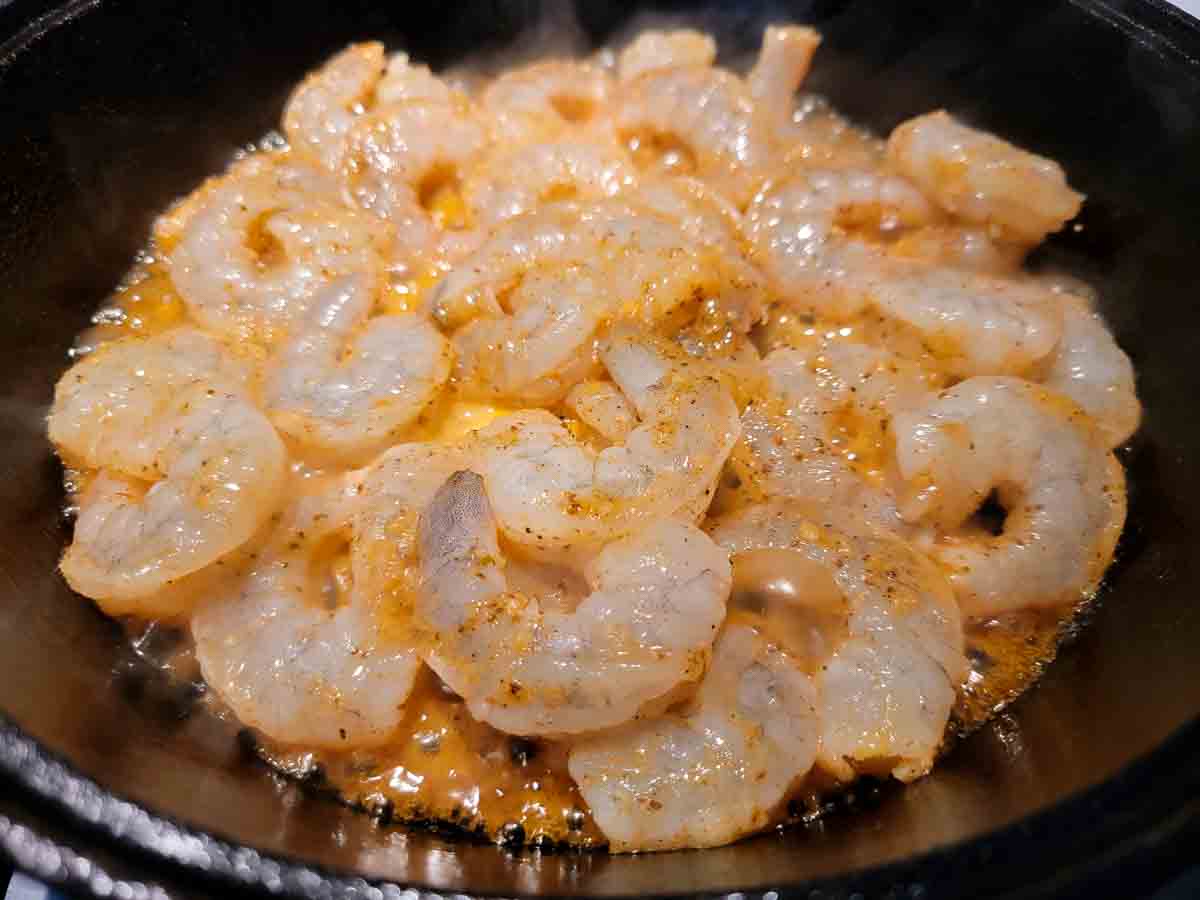 shrimp, honey, butter, Old Bay seasoning, garlic, and ginger cooking in a cast iron skillet.