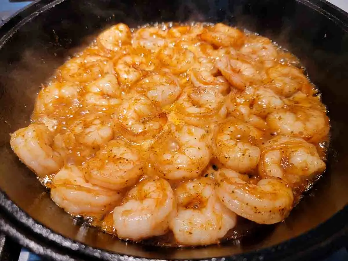 shrimp, honey, butter, Old Bay seasoning, garlic, and ginger cooking in a cast iron skillet.