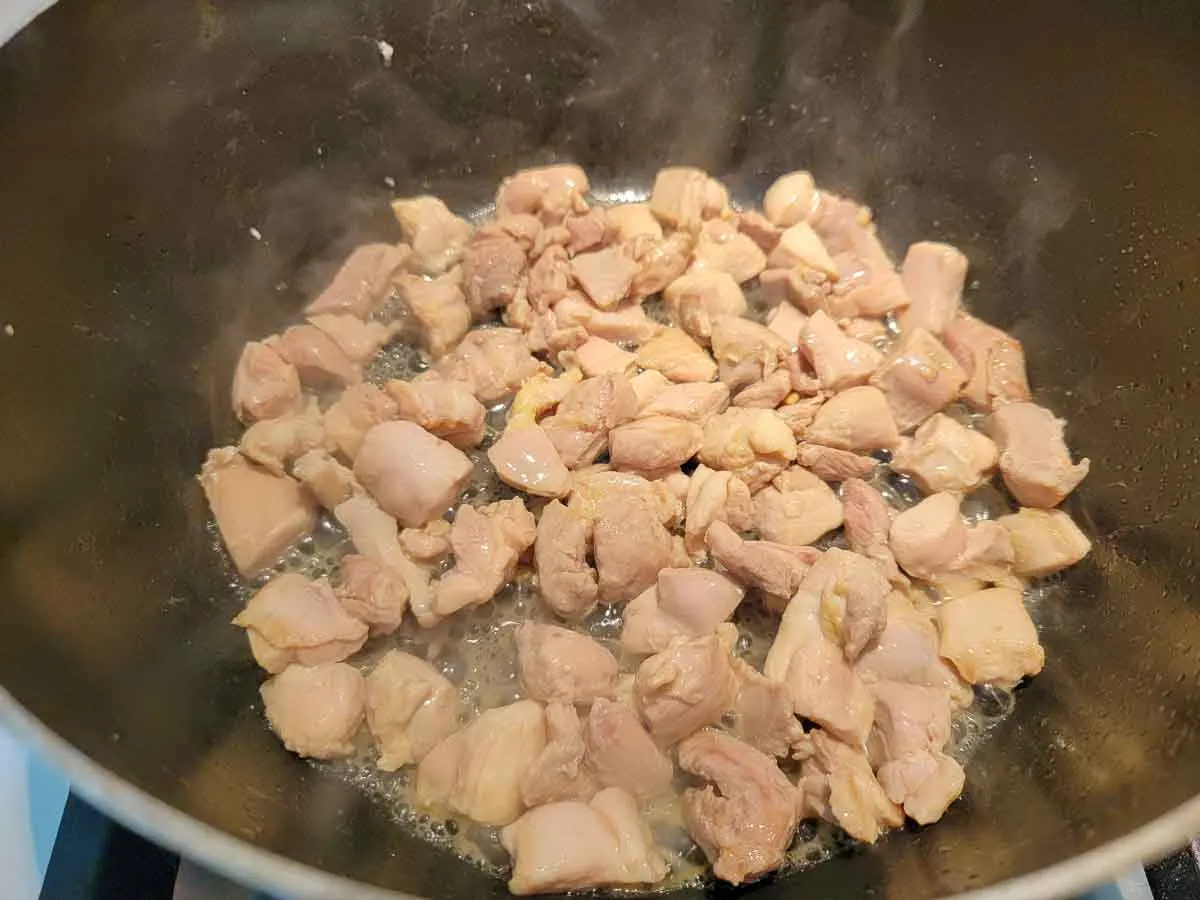 cubed chicken thighs cooking in a pan.