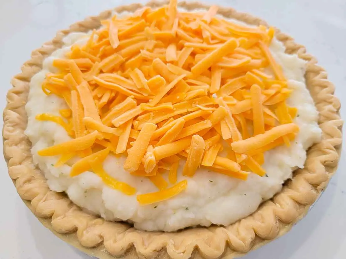 cottage pie filling topped with mashed potatoes and cheddar cheese in a pie crust.