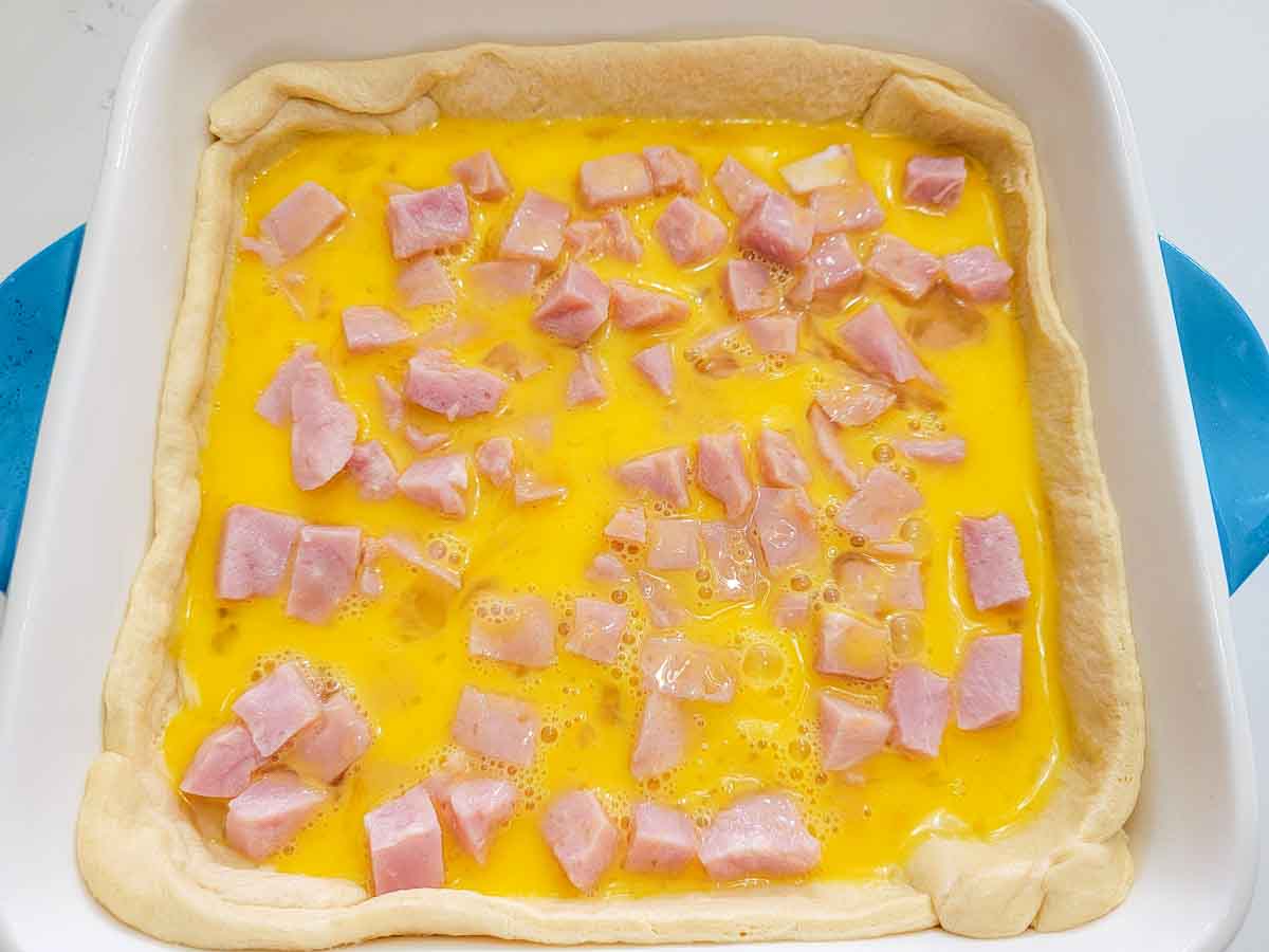 beaten egg and diced ham layered over crescent dough in a baking dish.